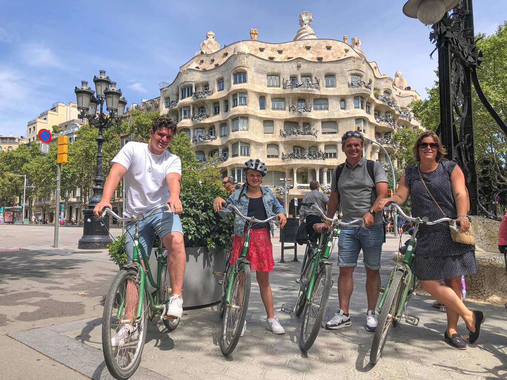 Een vrolijk gezin met tieners poseert met fietsen voor Casa Mila in Barcelona.