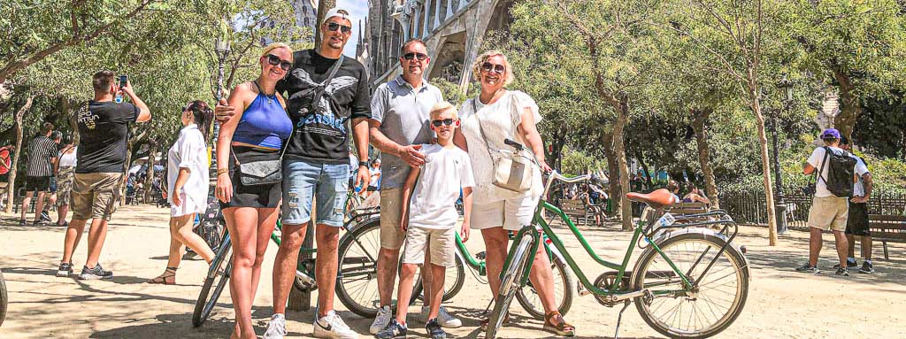 Family with children and young couple posing happily together with bikes in front of Sagrada Familia in Barcelona