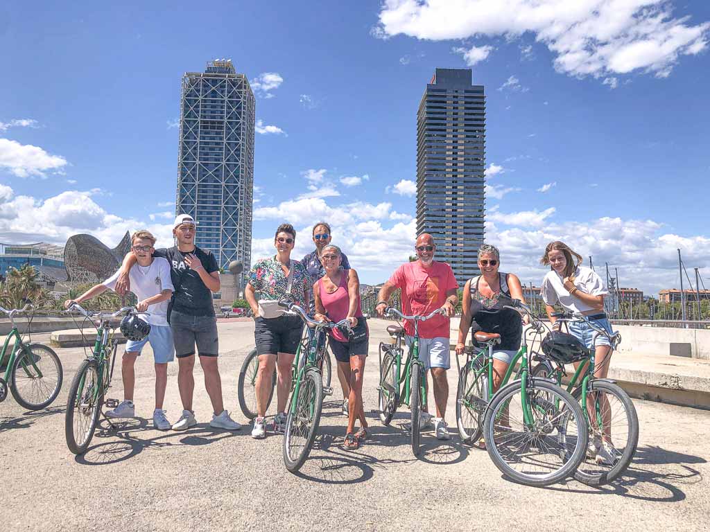 Vrolijke groep mensen poseert met groene fietsen bij de Olympische Haven in Barcelona tijdens een zomerdag tijdens de Barcelona Highlights Tour van Perry Tours.