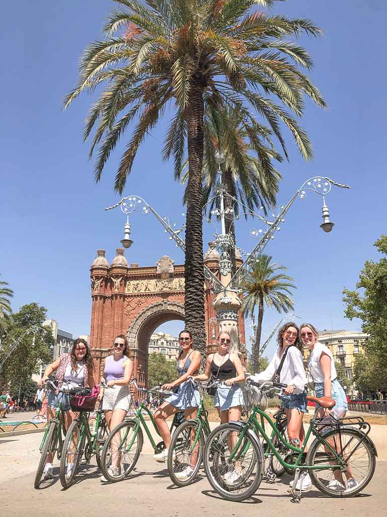 Groep meiden poseert met fietsen voor de Arc de Triomf tijdens een fietstocht met Perry Tours op een zonnige dag vol plezier.