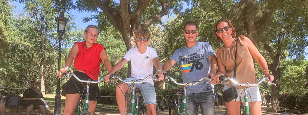 Vier gezinsleden poseren met hun fietsen in de schaduw van bomen in een park in Barcelona.